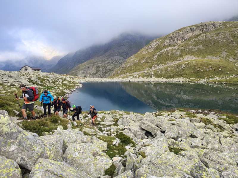 Il gruppo risale lungo il lago, con il rifugio in lontananza tra le nuvole