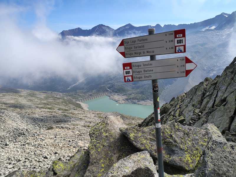 I cartelli del sentiero 601, con il grande lago e la diga sullo sfondo